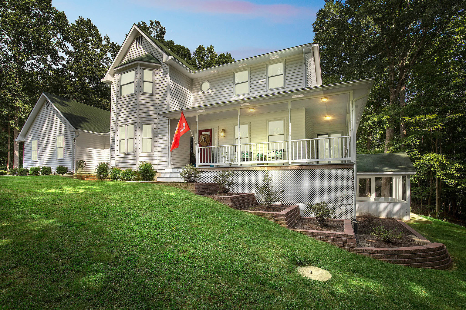 Home photograph supplied for the Saint Leonard community guide, showing a white house with a covered porch and wooded surroundings